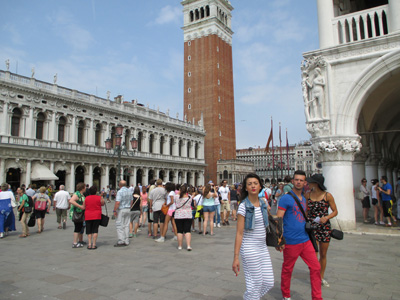Photo shows crowded plaza with a red brick tower in the background, about 8 stories high.